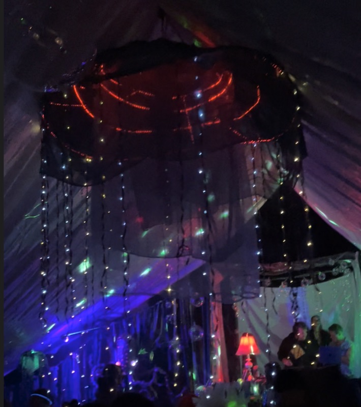 A glowing jellyfish-shaped canopy hung inside a tent, trailing strings of lights down over a crowd
