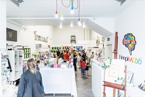 The Happimess studio in Squamish, a bright white room strung with coloured pendant lights, tables of art materials and people browsing